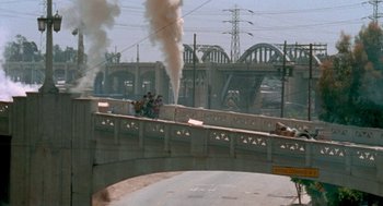 Movie still from “Jackass: The Movie” (2002), directed by Jeff Tremaine – Smoke billows from a bridge over a river; Extreme Wide shot, High angle