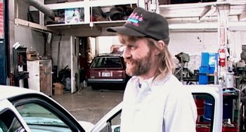 Movie still from “Jackass: The Movie” (2002), directed by Jeff Tremaine – A man with long hair wearing a hat and smiling; Medium shot, Over the shoulder angle