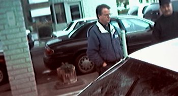 Movie still from “Jackass: The Movie” (2002), directed by Jeff Tremaine – A man standing in front of a car on the side of the road; Medium shot, High angle