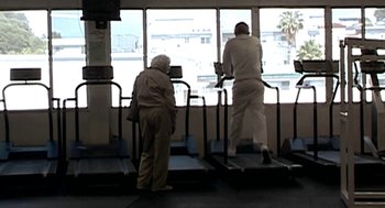 Movie still from “Jackass: The Movie” (2002), directed by Jeff Tremaine – Two older people are on a treadmill in a train; Wide shot, Low angle