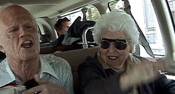 Movie still from “Jackass: The Movie” (2002), directed by Jeff Tremaine – An older woman sitting in the back seat of a car; Medium shot, Over the shoulder angle