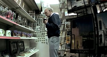 Movie still from “Jackass: The Movie” (2002), directed by Jeff Tremaine – An older man is looking at a shelf of glasses; Medium shot, High angle