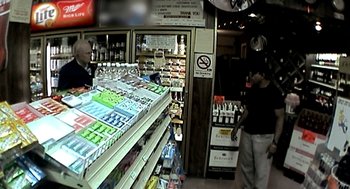 Movie still from “Jackass: The Movie” (2002), directed by Jeff Tremaine – A man standing in front of a store filled with lots of drinks; Wide shot, Over the shoulder angle