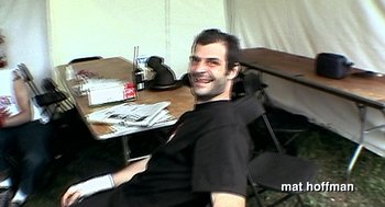 Movie still from “Jackass: The Movie” (2002), directed by Jeff Tremaine – A man sitting at a table in front of papers; Medium shot, High angle