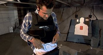 Movie still from “Jackass: The Movie” (2002), directed by Jeff Tremaine – A man in a vest is holding a knife and looking at a target; Medium shot, High angle