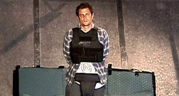 Movie still from “Jackass: The Movie” (2002), directed by Jeff Tremaine – A man wearing a body armor on a stage; Medium shot, Low angle