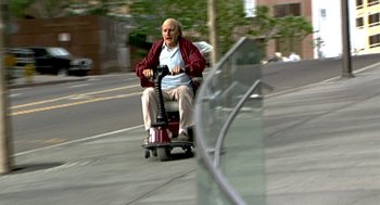 Movie still from “Jackass: The Movie” (2002), directed by Jeff Tremaine – An older man riding a scooter down a street; Wide shot, High angle