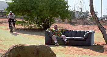 Movie still from “Jackass: The Movie” (2002), directed by Jeff Tremaine – A man sitting on top of a couch in a field; Wide shot, High angle