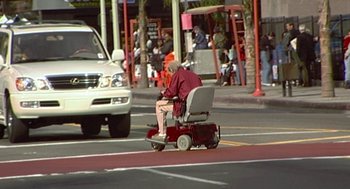 Movie still from “Jackass: The Movie” (2002), directed by Jeff Tremaine – An older man is sitting on a scooter on the street; Wide shot, High angle
