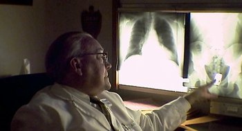Movie still from “Jackass: The Movie” (2002), directed by Jeff Tremaine – An older man sitting in front of an x - ray screen; Medium shot, Low angle
