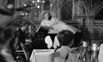 Movie still from “Jacquot of Nantes” (1991), directed by Agnès Varda – A woman sitting on top of a chair in a restaurant; Medium shot, Low angle