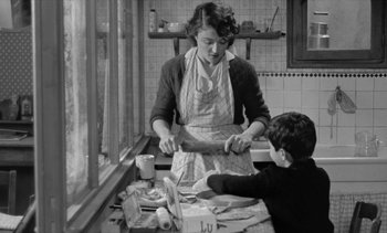 Movie still from “Jacquot of Nantes” (1991), directed by Agnès Varda – A woman and a boy in a kitchen preparing food; Medium shot, Low angle