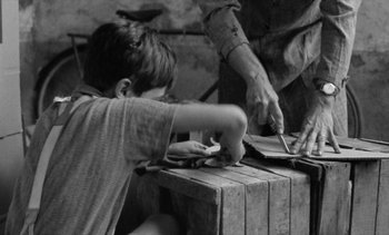 Movie still from “Jacquot of Nantes” (1991), directed by Agnès Varda – A man and a boy cutting paper with scissors; Medium shot, High angle