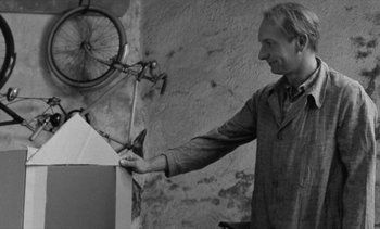 Movie still from “Jacquot of Nantes” (1991), directed by Agnès Varda – A black - and - white photo of a man holding a bicycle; Medium shot, Low angle
