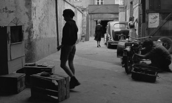 Movie still from “Jacquot of Nantes” (1991), directed by Agnès Varda – A man standing in the street with a knife in his hand; Wide shot, High angle