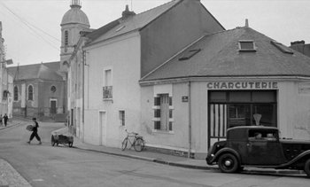 Movie still from “Jacquot of Nantes” (1991), directed by Agnès Varda – An old black and white photo of a street corner; Extreme Wide shot, Low angle