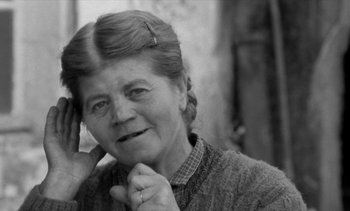 Movie still from “Jacquot of Nantes” (1991), directed by Agnès Varda – An older woman is smiling while holding her hand to her face; Close Up shot, Low angle
