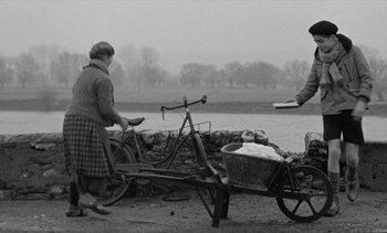 Movie still from “Jacquot of Nantes” (1991), directed by Agnès Varda – Two women pushing a bicycle with a cart full of food; Wide shot, Over the shoulder angle