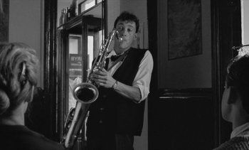 Movie still from “Jacquot of Nantes” (1991), directed by Agnès Varda – A man standing in a room holding a saxophone; Medium shot, Low angle
