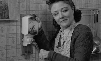 Movie still from “Jacquot of Nantes” (1991), directed by Agnès Varda – An old photo of a woman putting money in a coin dispenser; Medium shot, Low angle