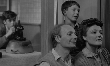 Movie still from “Jacquot of Nantes” (1991), directed by Agnès Varda – An older man and two young boys are smiling for the camera; Medium shot, Over the shoulder angle
