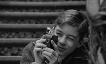 Movie still from “Jacquot of Nantes” (1991), directed by Agnès Varda – A young man taking a picture with a camera; Close Up shot, High angle