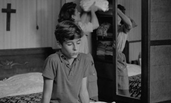 Movie still from “Jacquot of Nantes” (1991), directed by Agnès Varda – A young boy sitting in front of a mirror; Medium shot, Over the shoulder angle