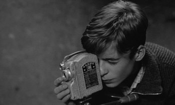Movie still from “Jacquot of Nantes” (1991), directed by Agnès Varda – A young man holding an old camera in his hands; Close Up shot, High angle