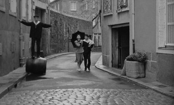 Movie still from “Jacquot of Nantes” (1991), directed by Agnès Varda – A man and a woman walking down a street holding an umbrella; Wide shot, High angle