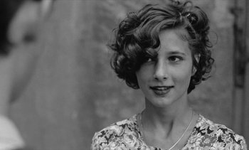 Movie still from “Jacquot of Nantes” (1991), directed by Agnès Varda – A young woman with short curly hair wearing a floral dress; Close Up shot, Over the shoulder angle