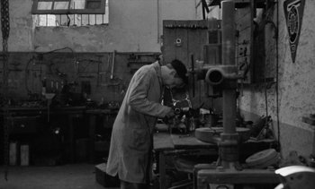 Movie still from “Jacquot of Nantes” (1991), directed by Agnès Varda – A man working in an industrial setting with a drill; Wide shot, High angle