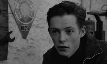 Movie still from “Jacquot of Nantes” (1991), directed by Agnès Varda – Black and white photograph of a young man in front of a wall; Close Up shot, Over the shoulder angle