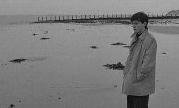 Movie still from “Jacquot of Nantes” (1991), directed by Agnès Varda – A man standing on the beach in front of a body of water; Medium shot, High angle