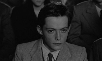 Movie still from “Jacquot of Nantes” (1991), directed by Agnès Varda – A man in a suit and tie looking at the camera; Close Up shot, High angle