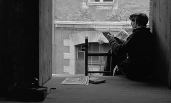 Movie still from “Jacquot of Nantes” (1991), directed by Agnès Varda – A person sitting on a chair reading a newspaper; Medium shot, High angle