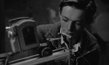 Movie still from “Jacquot of Nantes” (1991), directed by Agnès Varda – A young man is looking at an object on a table; Close Up shot, Low angle