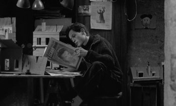 Movie still from “Jacquot of Nantes” (1991), directed by Agnès Varda – A man sitting at a table holding a magazine; Medium shot, High angle