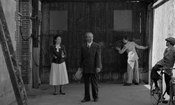 Movie still from “Jacquot of Nantes” (1991), directed by Agnès Varda – A man and a woman standing next to a man holding a tennis racquet; Wide shot, Low angle