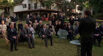 Movie still from “Jagged Edge” (1985), directed by Richard Marquand – A group of people sitting on lawn chairs in front of a building; Wide shot, High angle
