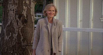 Movie still from “Jagged Edge” (1985), directed by Richard Marquand – A woman standing next to a tree smiling for the camera; Medium shot, Low angle