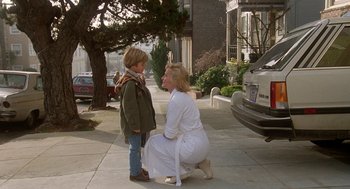 Movie still from “Jagged Edge” (1985), directed by Richard Marquand – A woman kneeling down next to a boy on a sidewalk; Wide shot, Over the shoulder angle