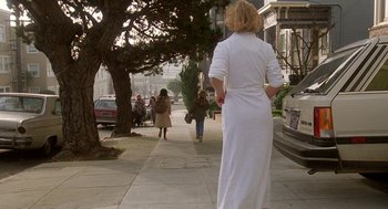Movie still from “Jagged Edge” (1985), directed by Richard Marquand – A woman in a white dress walking down a sidewalk; Wide shot, Low angle