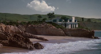 Movie still from “Jagged Edge” (1985), directed by Richard Marquand – A house sitting on top of a hill next to the ocean; Extreme Wide shot, High angle