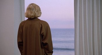 Movie still from “Jagged Edge” (1985), directed by Richard Marquand – A woman in a brown jacket looking out at the ocean; Medium shot, High angle