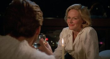 Movie still from “Jagged Edge” (1985), directed by Richard Marquand – A woman sitting in front of a lit candle in front of another woman; Close Up shot, Over the shoulder angle