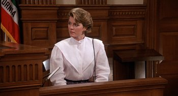 Movie still from “Jagged Edge” (1985), directed by Richard Marquand – A woman sitting in a court room wearing a white shirt; Medium shot, Over the shoulder angle
