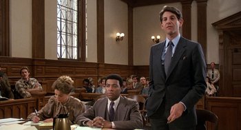 Movie still from “Jagged Edge” (1985), directed by Richard Marquand – A man in a suit stands in front of two other men in a courtroom; Medium shot, Low angle