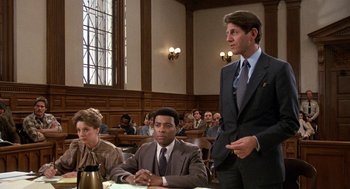 Movie still from “Jagged Edge” (1985), directed by Richard Marquand – A man in a suit stands in front of two other men in a courtroom; Medium shot, Low angle