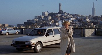 Movie still from “Jagged Edge” (1985), directed by Richard Marquand – A woman standing in front of a white car in a parking lot; Wide shot, High angle