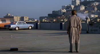 Movie still from “Jagged Edge” (1985), directed by Richard Marquand – A man standing in a parking lot next to a white car; Wide shot, High angle